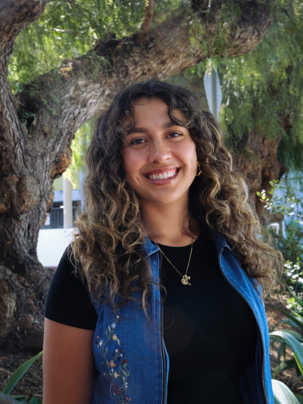 Abigail Garewal, smiling, photographed outdoors under a willow tree
