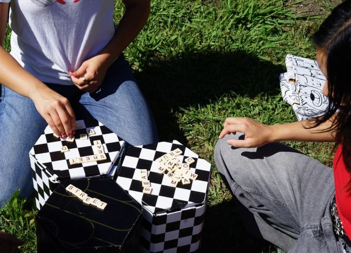 Two people playing Scrabble on top of a Street Seat, tiles spelling STREET and SEAT