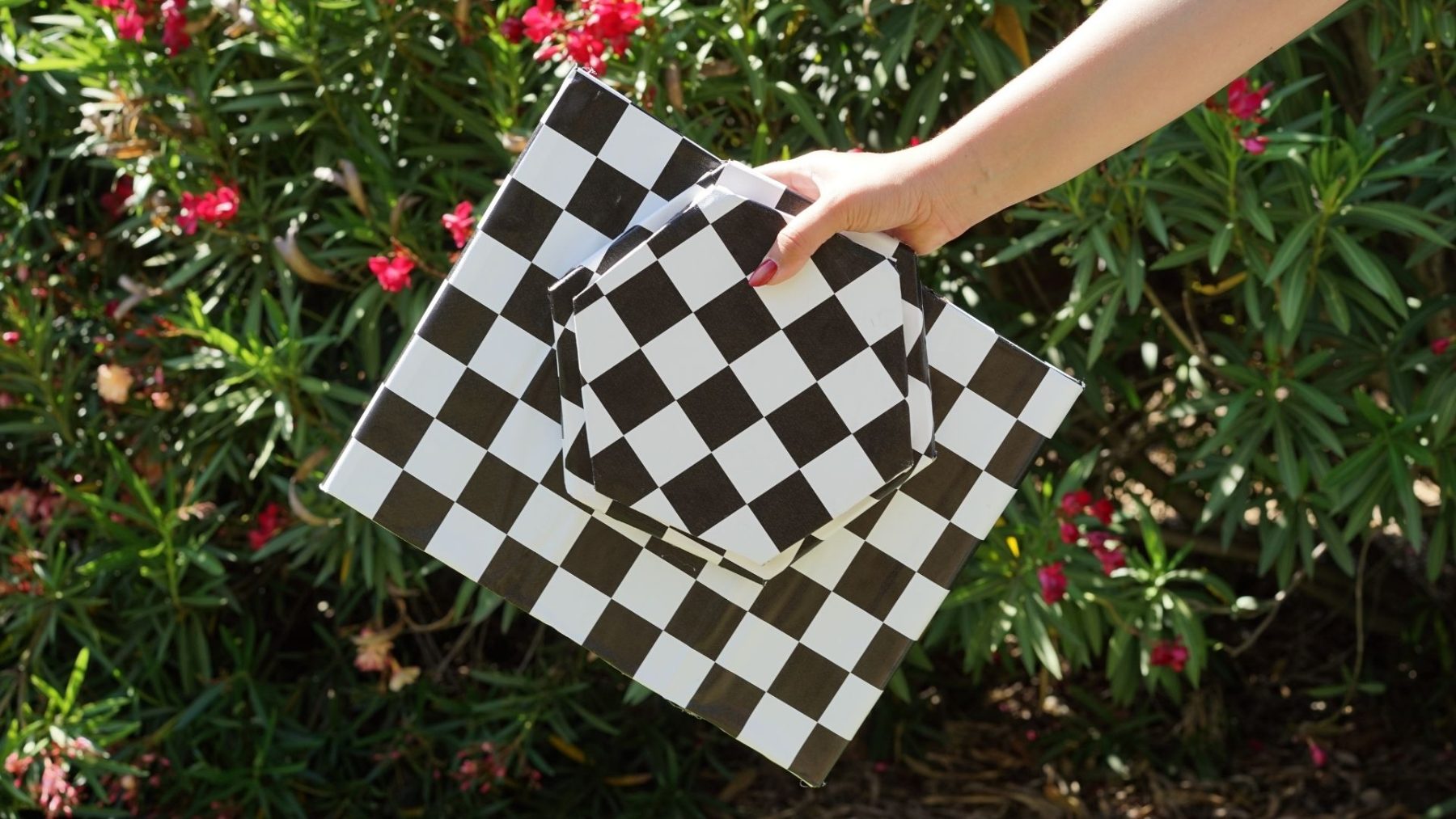 Hand holding the checkerboard-wrapped Street Seat panels, flat-packed against red flowers