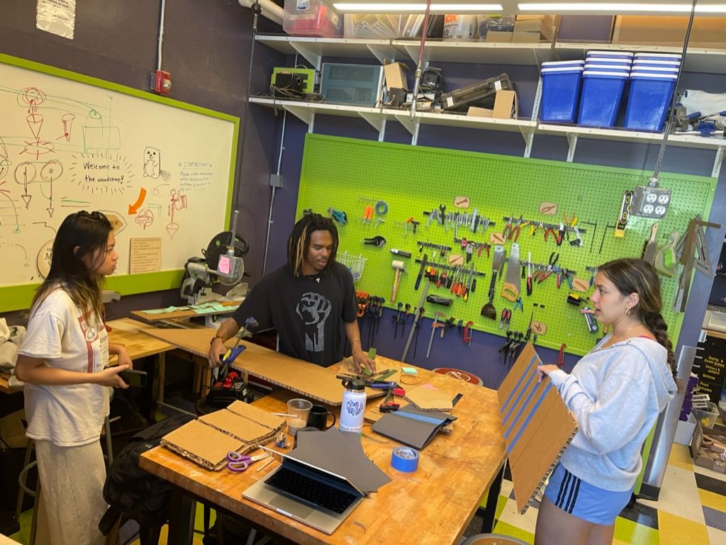 Three students at a green pegboard workbench, planning the build