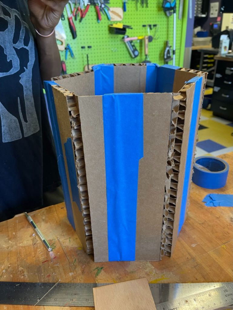 Tape-wrapped hexagonal cardboard prototype standing on the bench